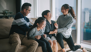 Image shows a happy family together laughing. Two parents and two children.