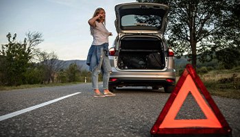 a woman on the side of the road with reflectors up after her car breaks down on the road